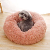 Small gray dog resting in a round pink fluffy pet bed on a wooden floor
